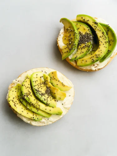 Tostadas integrales con crema untable, rodajas de aguacate fresco y semillas de chía sobre una superficie clara.