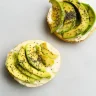 Tostadas integrales con crema untable, rodajas de aguacate fresco y semillas de chía sobre una superficie clara.