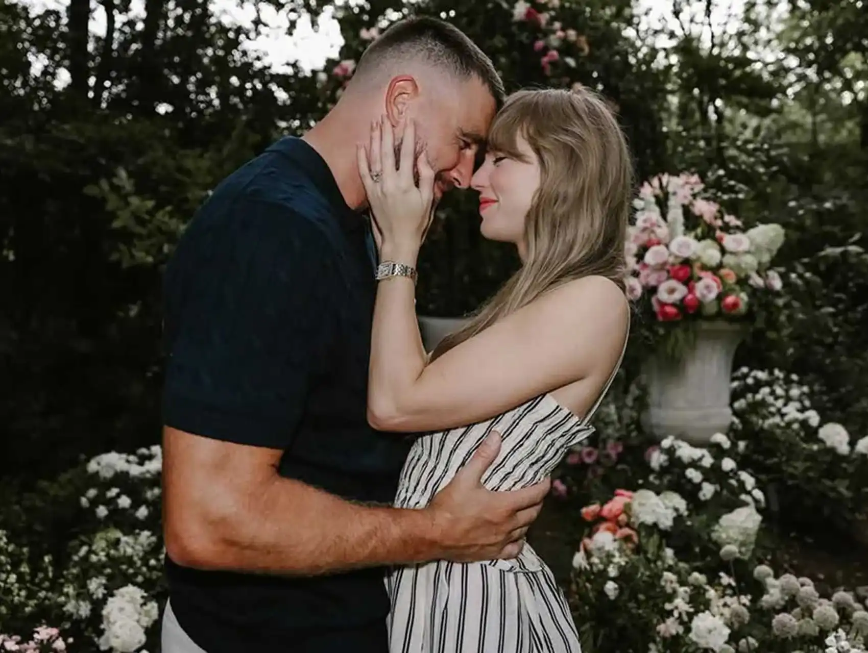 Taylor Swift with her fiancé in a garden, showing her naked engagement nails and diamond ring.