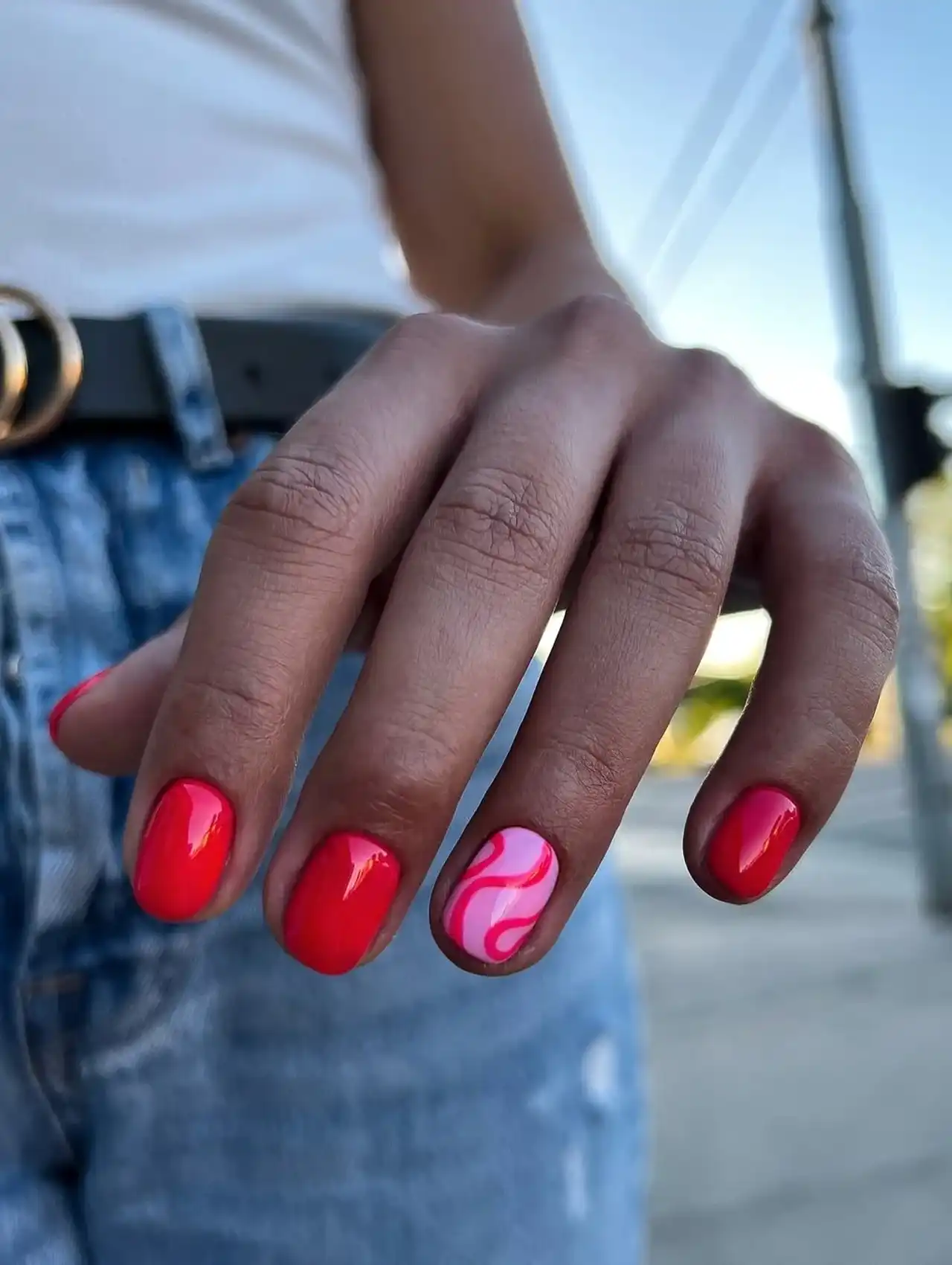 Uñas de Tendencia con esmalte rojo y diseño de ondas rosas en dedo anular