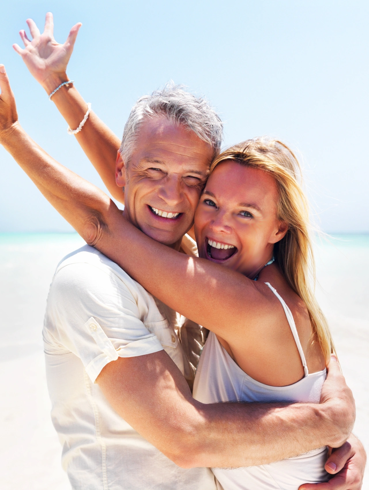Pareja abrazándose en la playa con alegría, representando la conexión emocional clave para cómo enamorar a una mujer siendo mayor.