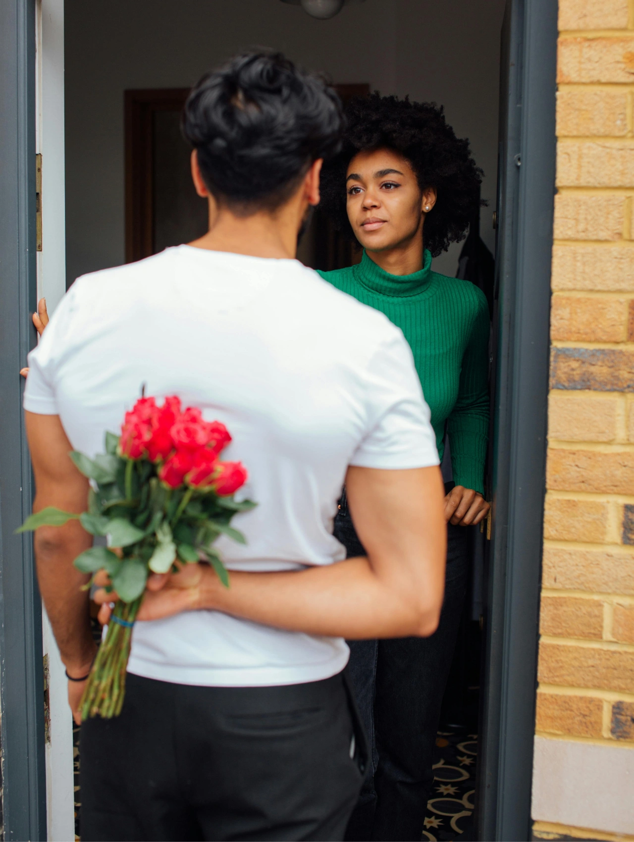 Hombre con flores ocultas detrás de la espalda frente a una mujer en la puerta, ejemplo de frases para enamorar a una mujer en la madurez.