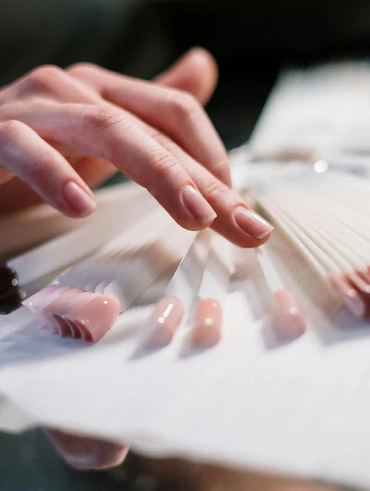 Hand selecting from different topcoat nail polish samples in soft pink shades.