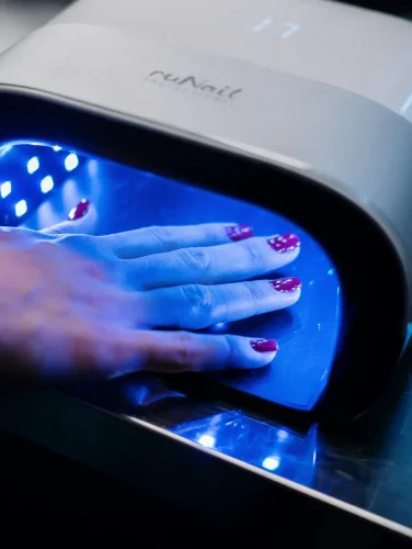 Hand curing red topcoat nail polish under a UV LED lamp.