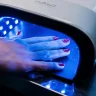Hand curing red topcoat nail polish under a UV LED lamp.
