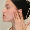 Young woman with calm dewy complexion gently pressing the best skincare for sensitive skin onto her cheek after cleansing