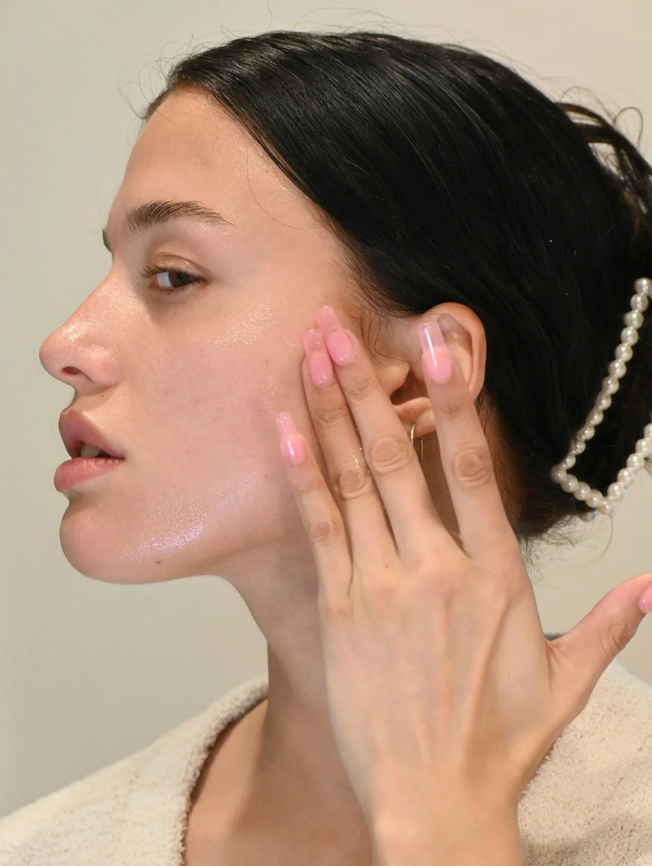 Young woman with calm dewy complexion gently pressing the best skincare for sensitive skin onto her cheek after cleansing