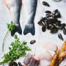 Fresh sea bass, mussels, prawns and parsley laid out on marble, the raw ingredients for a delicious gourmet meal