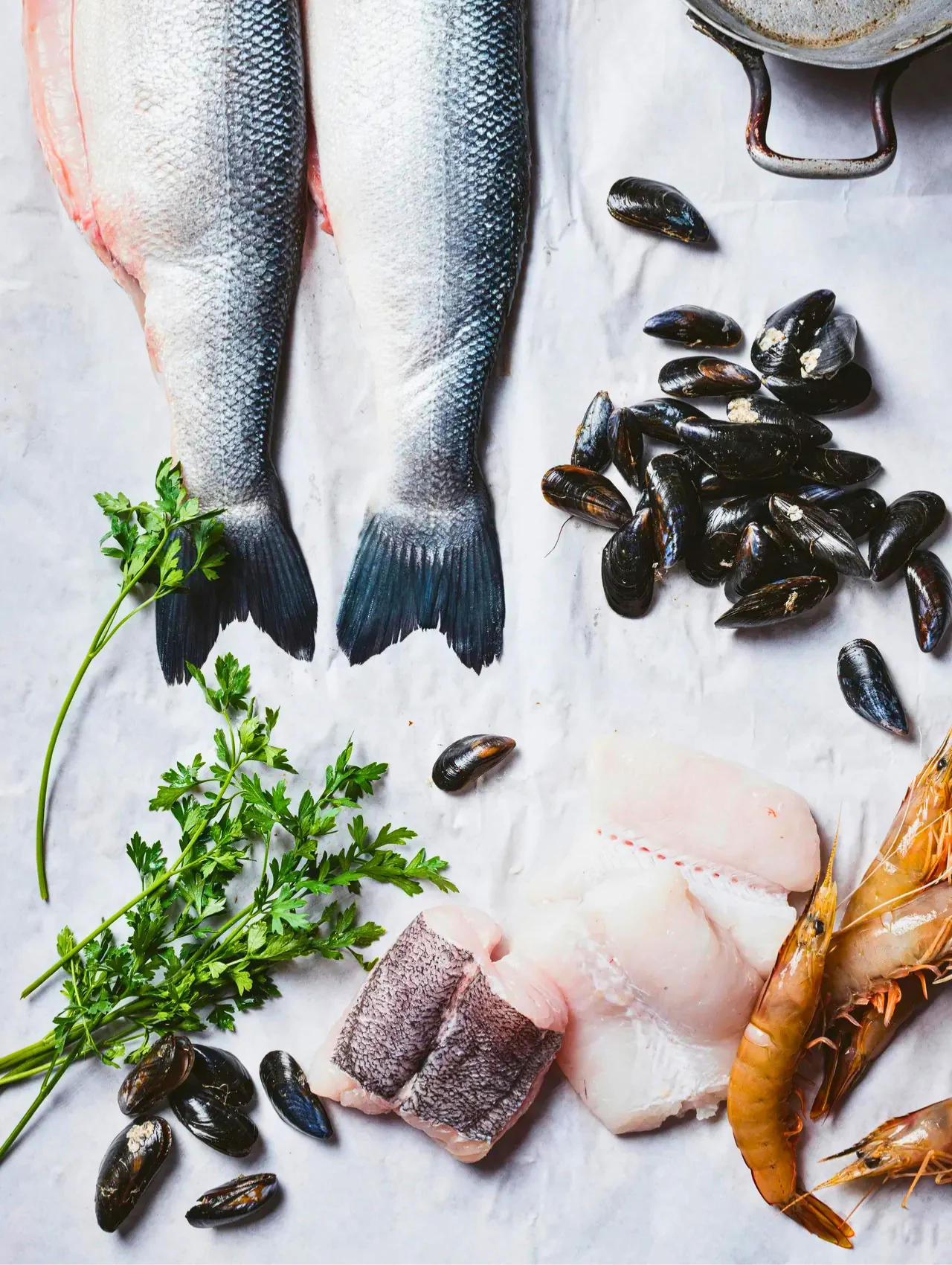 Fresh sea bass, mussels, prawns and parsley laid out on marble, the raw ingredients for a delicious gourmet meal